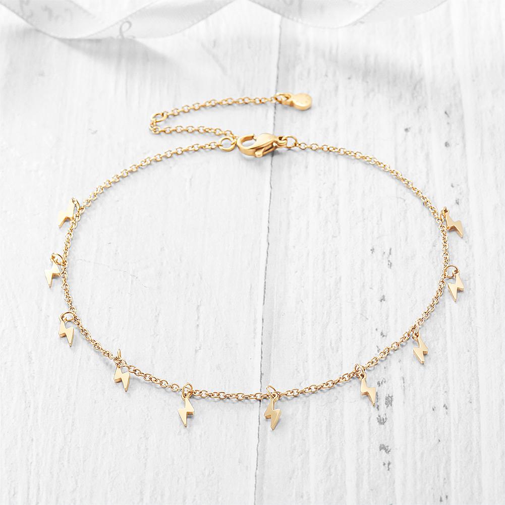 Gold lightning charm anklet laid flat on white wood – dainty and edgy jewelry for women.